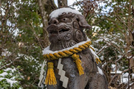 Komainu, or lion-dog, statue in winter snow with sacred shimenawa rope at small local shrine, Kanazawa, Japan.