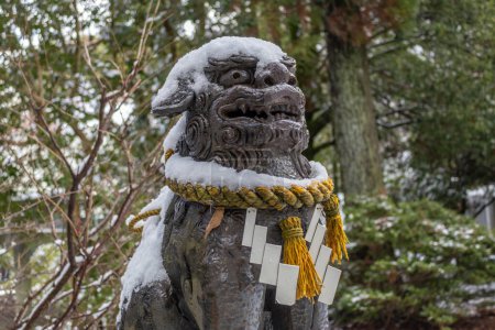 Komainu, oder Löwenhund, Statue im Winterschnee mit heiligem Shimenawa-Seil am kleinen lokalen Schrein, Kanazawa, Japan.