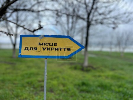 Foto de Puntero-Placa (camino al refugio antibombas) contra el fondo de los árboles otoñales y el cielo azul. Traducción: "Lugar de refugio". Guerra en Ucrania - Imagen libre de derechos