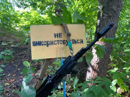 Foto de El rifle de asalto Kalashnikov cuelga cerca de un árbol con una inscripción. Traducción: "No te inclines". Guerra en Ucrania - Imagen libre de derechos