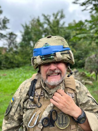 Foto de Retrato, mueca de un anciano soldado ucraniano en casco con franja azul, uniforme de soldado del ejército ucraniano - Imagen libre de derechos