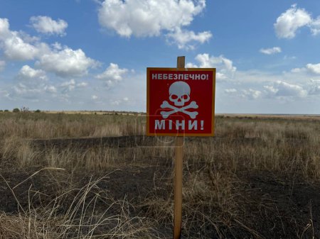 Foto de Señal de peligro mina en ucraniano cerca de un campo agrícola durante la guerra en Ucrania, traducción: "Peligro de minas" - Imagen libre de derechos
