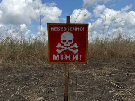 Foto de Señal de peligro mina en ucraniano cerca de un campo agrícola durante la guerra en Ucrania, traducción: "Peligro de minas" - Imagen libre de derechos