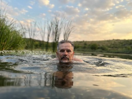 Foto de Anciano de pelo gris con barba se alegra de que acaba de salir del agua del río contra el telón de fondo de cañas verdes en la noche de verano - Imagen libre de derechos