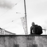 A young man is resting at Riga, Latvia. He is sitting on a concrete wall with his backpack.