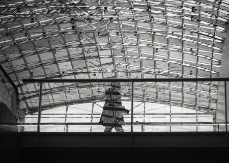 Photo for A man is walking by a big glass and steel ceiling. His shadow is reflected to the glass railing. - Royalty Free Image