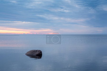 Photo for A lonely rock standing in the sea water at Kalajoki, Finland. The sun sets beautifully into the sea in the background. - Royalty Free Image