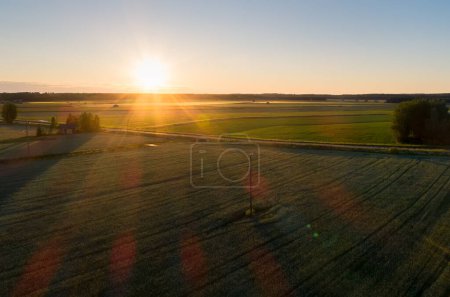 Photo for Mist rises from the fields while the sun is setting. The sunlight creates shadows of the telephone lines on the fields. - Royalty Free Image