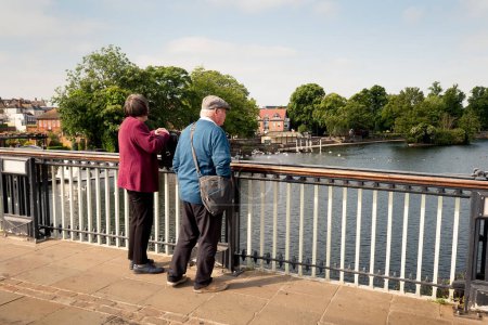 Photo for An elderly couple seems to be feeding the swans on the river from an old bridge in Windsor. - Royalty Free Image