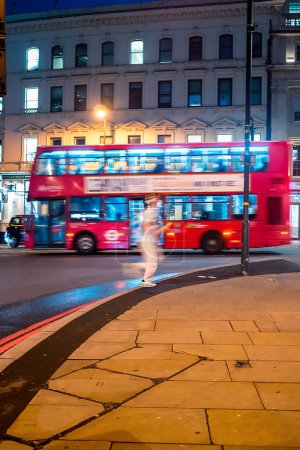 Photo for A person in white sporting clothes is running at a crossing in London. There's a double decker bus goiing by behind the runner. - Royalty Free Image