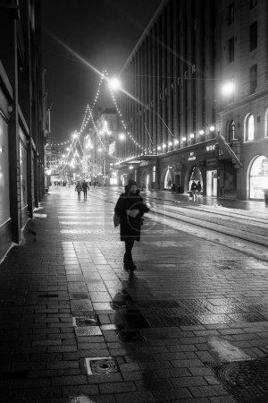 Photo for A woman is walking alone on a street decorated with Christmas lights on a winter night. - Royalty Free Image