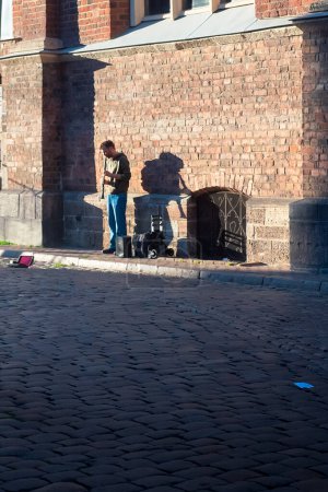 Photo for A man is playing clarinet by an old church at the old town of Riga, Latvia. - Royalty Free Image