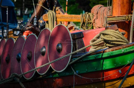 Close-up of a moored replica viking ship showing anchor rope and wooden shields in the morning sun