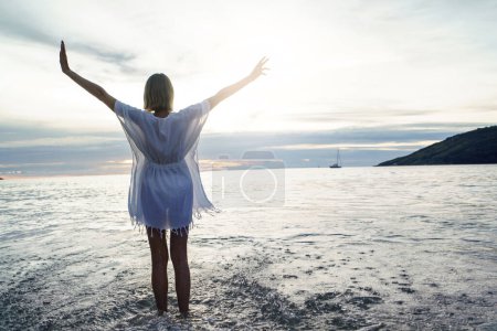 Téléchargez les photos : Vue arrière de la femme heureuse avec les mains en l'air profitant du coucher de soleil sur la plage. Voyage, concept de tourisme. Des vacances. Des vibrations insulaires. Thaïlande. - en image libre de droit