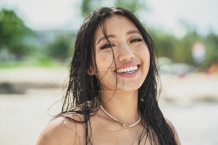 Téléchargez les photos : Une fille de l'île. Belle femme asiatique naturelle aux cheveux mouillés et au grand sourire en regardant la caméra, profitant d'une journée ensoleillée sur la plage. Des vibrations tropicales. Voyageur. La soif d'errance. Portrait beauté. - en image libre de droit