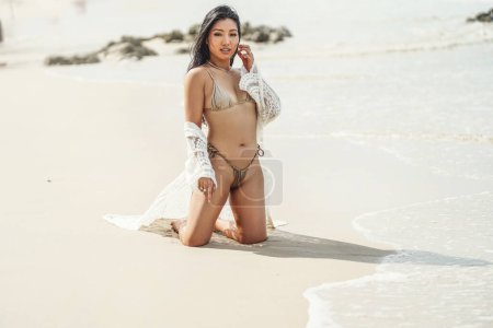Téléchargez les photos : Sexy belle femme asiatique en bikini à la mode relaxant sur la plage de sable, en regardant la caméra. Une photo pleine longueur. Espace de copie. Concept de voyage et de tourisme. - en image libre de droit
