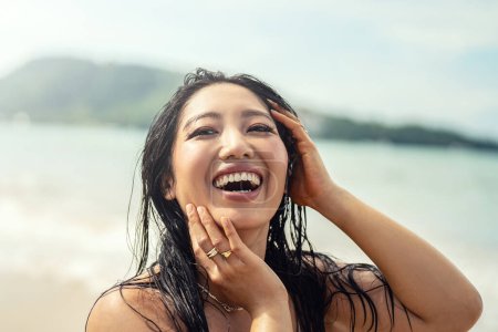Téléchargez les photos : Portrait de belle jeune femme asiatique avec un sourire de dents incroyable. Fille aux cheveux mouillés profitant d'une journée ensoleillée sur la plage. Bonne fête concept de style de vie. De vraies émotions. Voyageur - en image libre de droit
