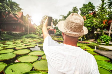Photo for Back view of a man in summer hat using cell phone to take selfie in beautiful place. Traveler. Tourism. Wanderlust. Asia - Royalty Free Image