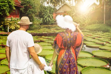 Téléchargez les photos : Vue arrière de la famille voyageant regardant un bel étang avec des fleurs de lotus géantes. Île tropicale. L'été. Style de vie des gens réels. - en image libre de droit