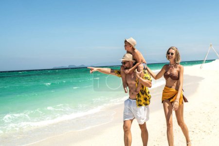 Foto de Joyful father, mother and son walking on the sandy tropical beach. Happy family holidays.  Active parents with children. Summer vibes. Copy space - Imagen libre de derechos