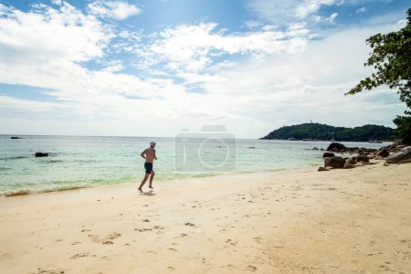 Téléchargez les photos : Sporty man running at the beach on sunny day. Fit male model working outdoor by the sea. Summer vibes, Tropics. - en image libre de droit