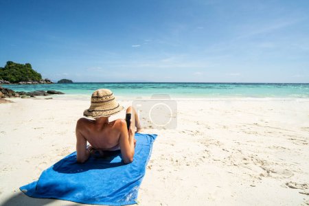 Foto de Back view photo of carefree happy female tourist realxing on the sandy beach, sunbating, enjoying summer tropical vacation. Island vibes. - Imagen libre de derechos