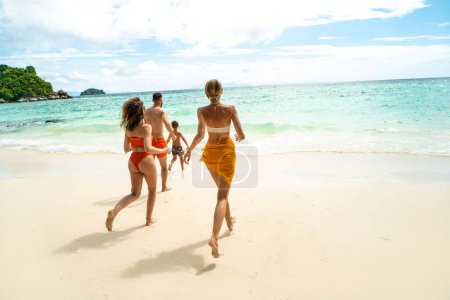 Foto de Back view of group of friends running to the tropical sea, having fun. Family vacation. Real people lifestyle. Summer vibes, Tropical island. - Imagen libre de derechos