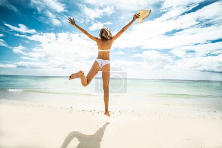 Photo for Happy young woman jumping on the beach. Back view. Full length photo. Summer vacation. Traveler. Tourism. - Royalty Free Image