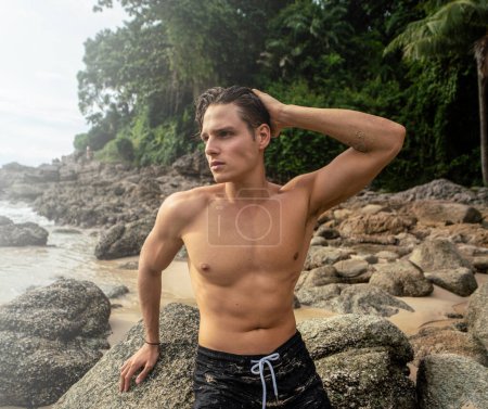 Téléchargez les photos : Fit young man posing shirtless on the tropical beach. Handsome guy relaxing on vacation. Summer time. Traveler. Tropical vibes. Wanderlust. - en image libre de droit