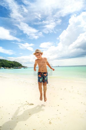 Foto de Happy child playing at the tropical sandy beach, jumping and having fun. Summer holiday. Leisure relax time. Tourism. Family vacation. - Imagen libre de derechos