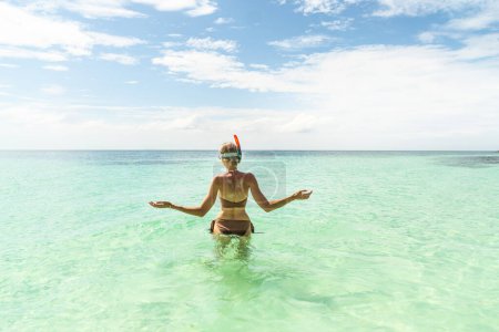 Foto de Woman in a brown bikini snorkeling on Maldives. Back view. Tropical coastline. Tourist. Traveler. Hobby. Wanderlust. Copy space - Imagen libre de derechos
