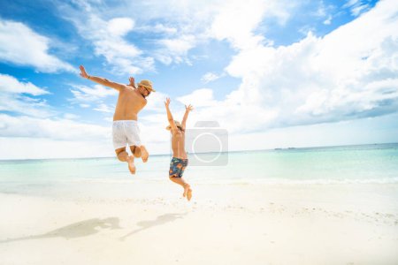 Photo for Happy family concept. Father and son jumping at the tropical beach, having fun together. Summer vacation. Happiness. Joy. Fun. Copy space. - Royalty Free Image
