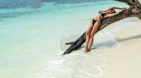 Téléchargez les photos : Fashion photo of beautiful tanned woman in black bikini relaxing and posing on wild tropical beach. Summer vibes. Wanderlust. - en image libre de droit