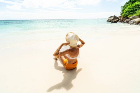 Foto de Model Girl in Sumer Hat Sun Tanning at the tropical beach with white sand. Summer Vacation. Holiday Travel. Tourism. Traveler. Back view. Copy space. - Imagen libre de derechos