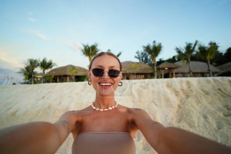 Photo for Young beautiful blonde woman in sunglasses smiling to the camera while taking selfie on the sandy tropical beach. Girl enjoying summer vacation concept. Travel. Tourist - Royalty Free Image