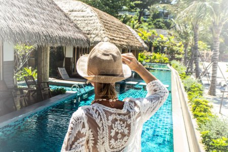 Téléchargez les photos : Femme détendue devant la maison tropicale et la piscine. Voyageuse dans une station balnéaire de luxe. Vacances et concept d'été. Style de vie des gens réels - en image libre de droit