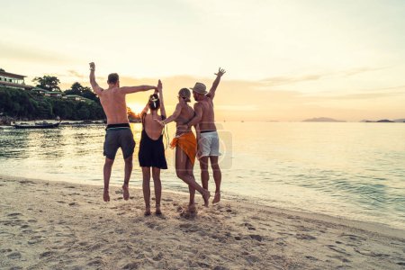 Photo for Group of happy friends enjoying beautiful sunset at the tropical beach, jumping and having fun together. Travelers. Tourism. Back view. Thailand, Asia. - Royalty Free Image