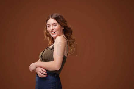 Photo for One of a kind, super natural, happy girl laughing to the camera. Real people emotions. Fun and joy. Beautiful woman with freckles on her face and body and long wavy hair. Brown studio background with a lot of copy space. - Royalty Free Image