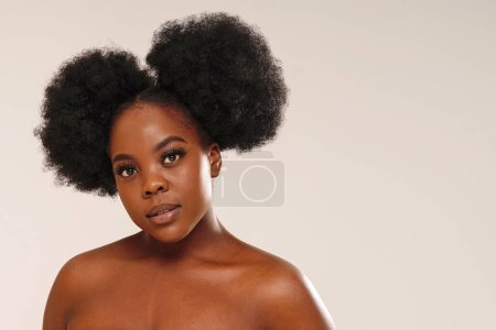 Foto de Retrato de belleza de mujer atractiva con cabello afro mirando a la cámara, posando sobre fondo de estudio. Chica con pestañas largas y maquillaje delicado. Un montón de espacio de copia - Imagen libre de derechos