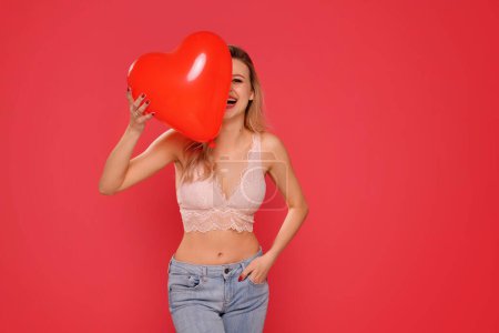 Foto de Mujer feliz con el corazón globo rojo riendo y divirtiéndose, de pie sobre el fondo del estudio rojo. Auto-amor, concepto de cuidado de la piel. Copiar espacio. - Imagen libre de derechos