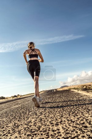 Foto de Vista trasera de la joven en forma femenina corriendo en el día soleado, luz de la mañana. Motivación, fitness y estilo de vida saludable. - Imagen libre de derechos
