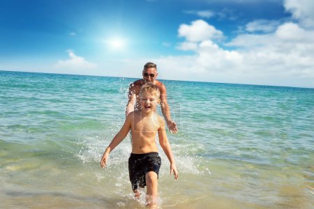 Photo for Family day. Happy dad and child having fun together outdoors, splashing sea water and laughing. Childhood and parenting concept - Royalty Free Image