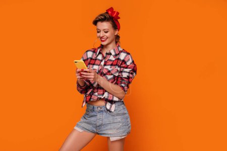 Photo for Studio Shot Of Smiling, Happy, Young Woman Using Mobile Phone, scrolling social media. Orange studio background. A lot of copy space. Internet addiction - Royalty Free Image