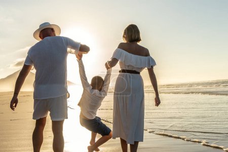 Téléchargez les photos : Joyeux concept de famille. Père, mère et fils s'amusent ensemble en été, plage au coucher du soleil. Vue arrière. - en image libre de droit