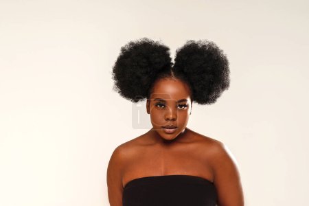 Foto de Retrato de belleza de una mujer linda con cabello afro mirando a la cámara, posando sobre el fondo del estudio. Chica con pestañas largas y maquillaje delicado. Un montón de espacio de copia - Imagen libre de derechos