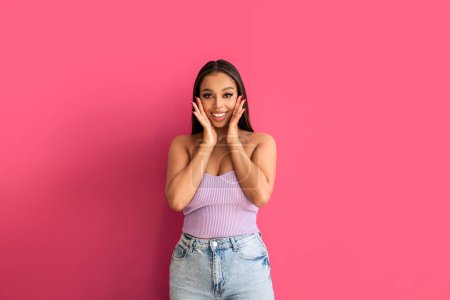 Photo for Joyful woman smiling, looking at the camera, posing on a pastel pink Studio Background. Real people emotions, toothy smile. Fashionable young girl in violet top and jeans.. A lot of copy space. - Royalty Free Image