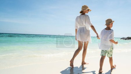 Foto de Vista trasera de madre e hijo felices caminando, relajándose en la playa de arena tropical, disfrutando de la vida. Día de verano. Vacaciones. Viajes. - Imagen libre de derechos