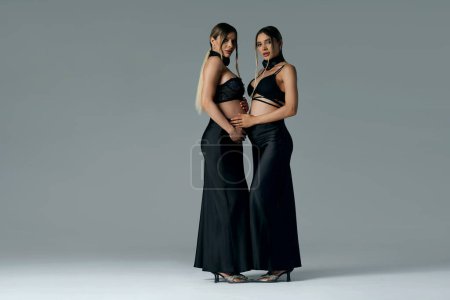 Photo for Photo of elegant pregnant young women, twins sisters. Studio shot of a ladies who are expecting babies. Free space for text. Full length photo. - Royalty Free Image