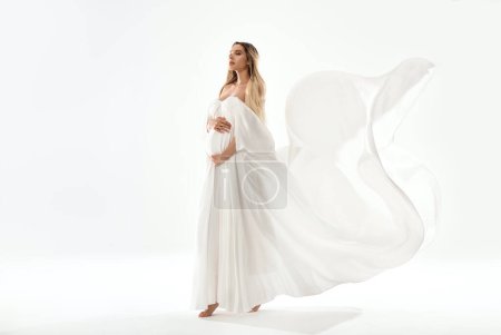 Photo for Delicate Pregnant Woman holding  her Belly wearing white, long Dress. Happy mom to be. A lot of copy space. Full length photo. - Royalty Free Image