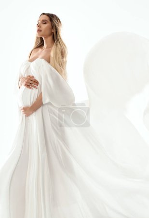 Foto de Mujer embarazada delicada sosteniendo su vientre vistiendo blanco, vestido largo. Feliz mamá por serlo. Un montón de espacio de copia. Foto de cuerpo entero. - Imagen libre de derechos
